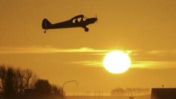 A small airplane flying near the sun with a clear sky.