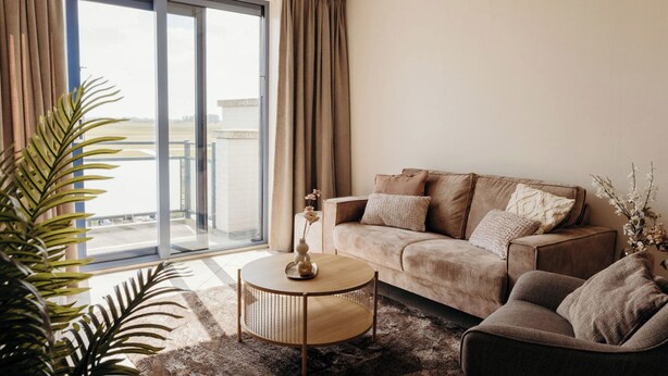 A modern living room with a sofa, a coffee table, and a view through a sliding glass door to an outdoor balcony. - Apartment in Netherlands Near the Coast (De Cocksdorp)