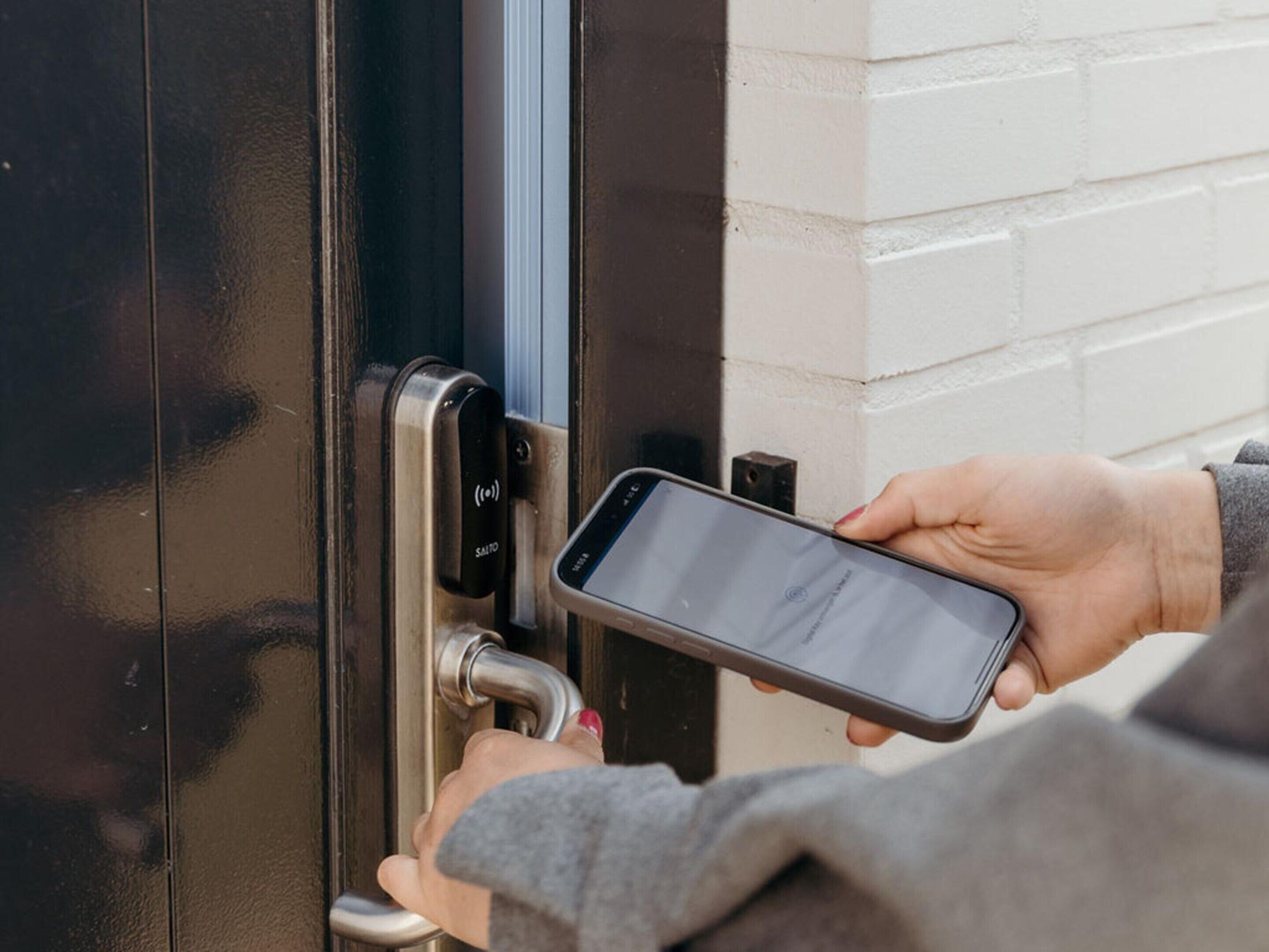 A person using a smartphone to interact with a door lock mechanism.