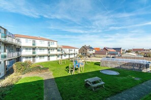En gårdhave med et legeområde, et overdækket drivhus og et picnicbord.