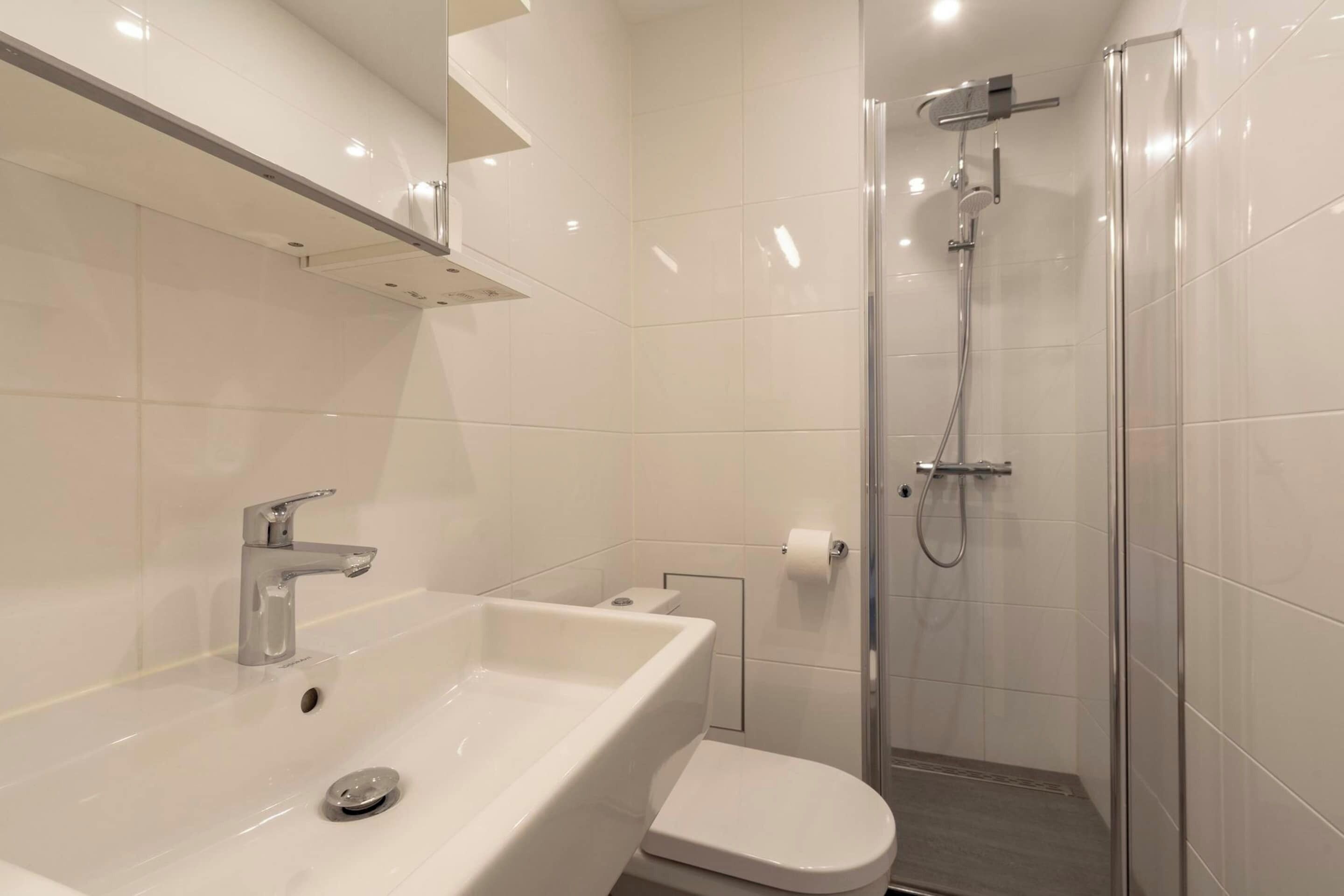 Een moderne badkamer met een wit wastafel, toilet en douche met glazen wanden.
