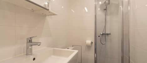Een moderne badkamer met een wit wastafel, toilet en douche met glazen wanden.