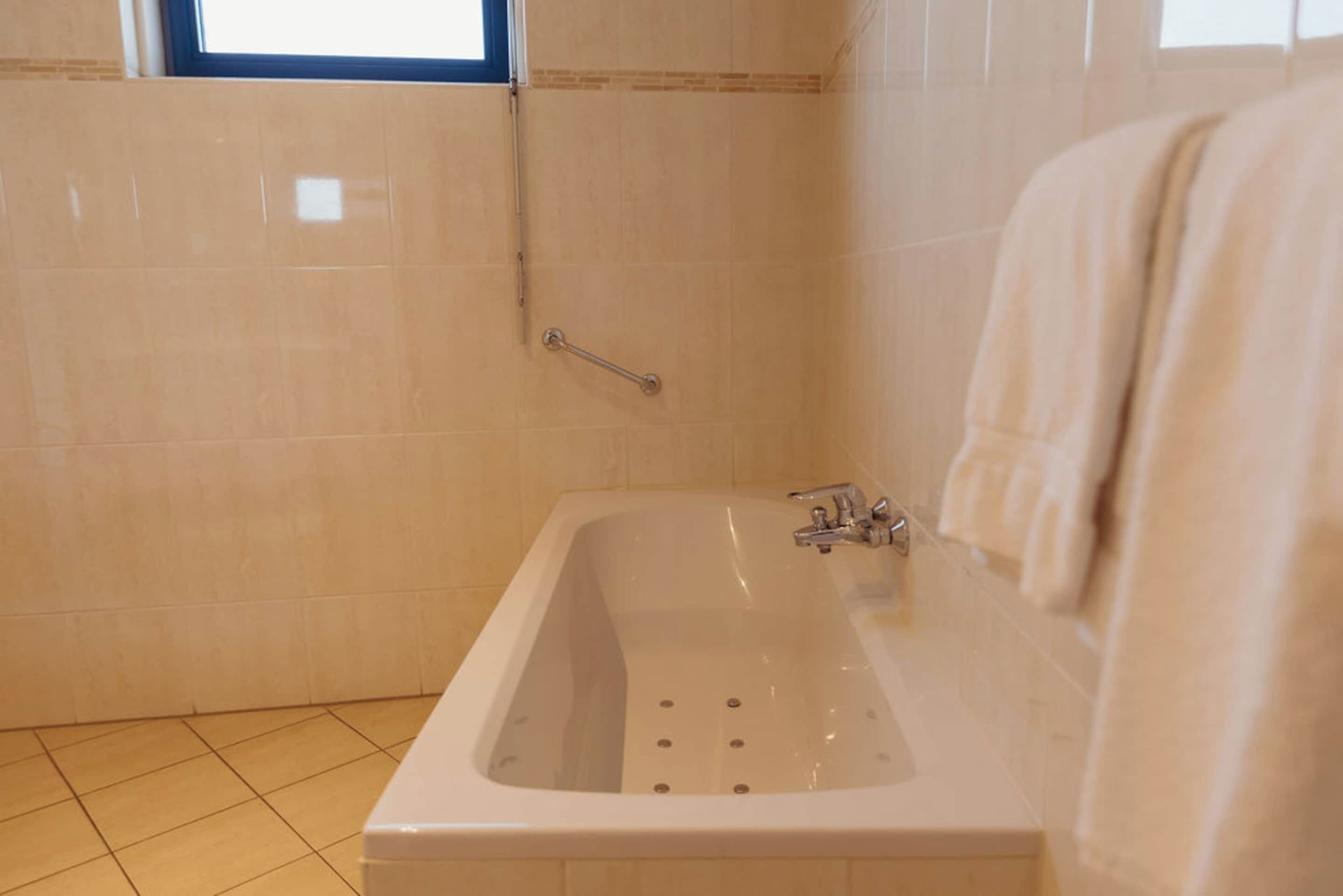 A bathroom with a bathtub, a handrail, and a window.