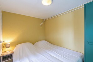 A small, single-bed room with a wooden nightstand, a lamp, and a teal door.