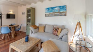 A living room with a sofa, coffee table, and chairs. There is a cabinet, a painting on the wall, and a lamp. - Duinland 122 Bungalow foe 2-people (Sint Maartensvlotbrug)
