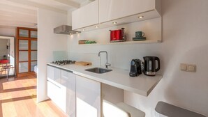 A modern kitchen with white cabinets, a gas stove, a sink, and a coffee machine. - Duinland 122 Bungalow foe 2-people (Sint Maartensvlotbrug)