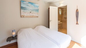 A bedroom with a bed, a painting of a beach, a fish decoration, and a bathroom door. - Duinland 122 Bungalow foe 2-people (Sint Maartensvlotbrug)