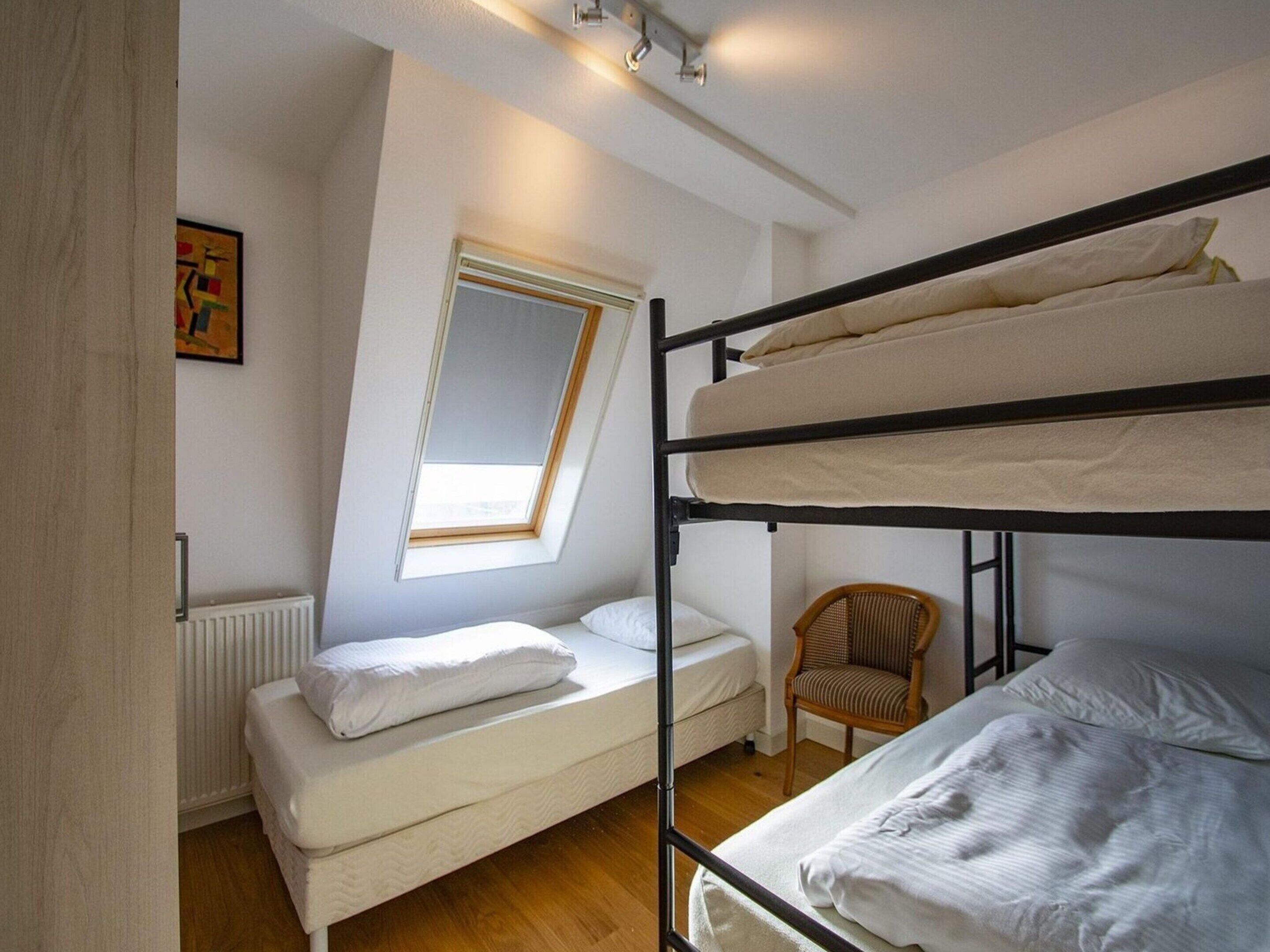Een slaapzaal met stapelbedden, een eenpersoonsbed, een stoel, een radiator en een dakvenster.