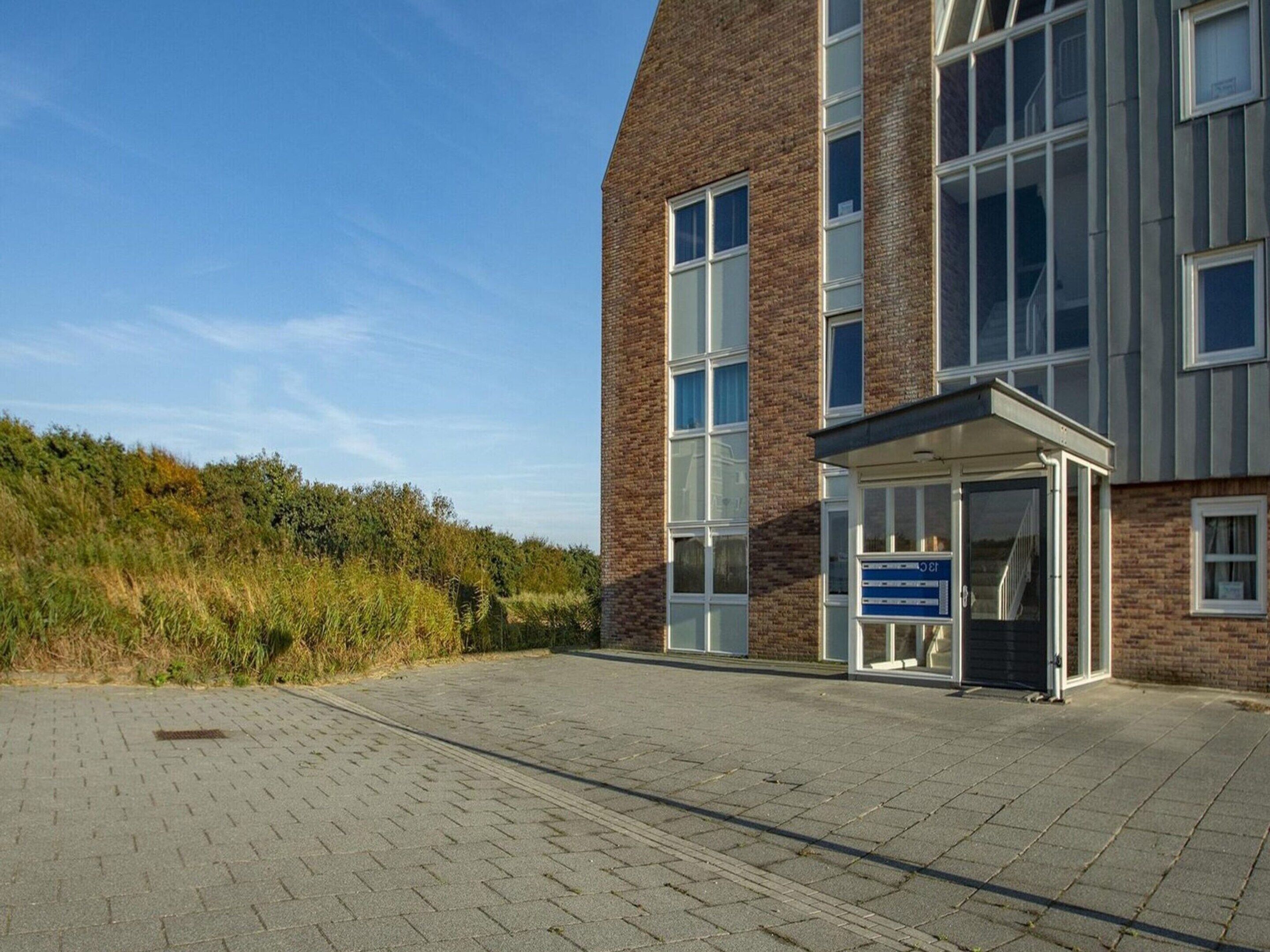 En moderne bygning med facade i mursten, store vinduer og et overdækket indgangsparti.