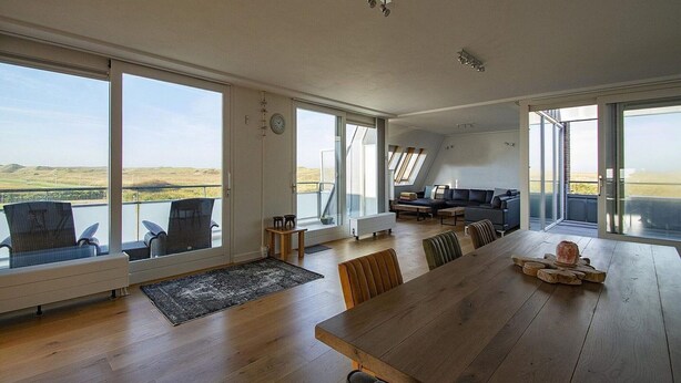 Ein großzügiges Wohnzimmer mit großen Fenstern, einem Essbereich und einer Sitzecke mit Landschaftsblick.