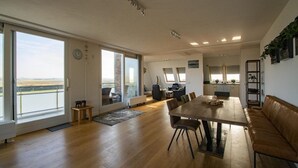 Ein großzügiger Wohnbereich mit einem großen Esstisch aus Holz, einem braunen Ledersofa und Blick auf die Landschaft durch große Glastüren.