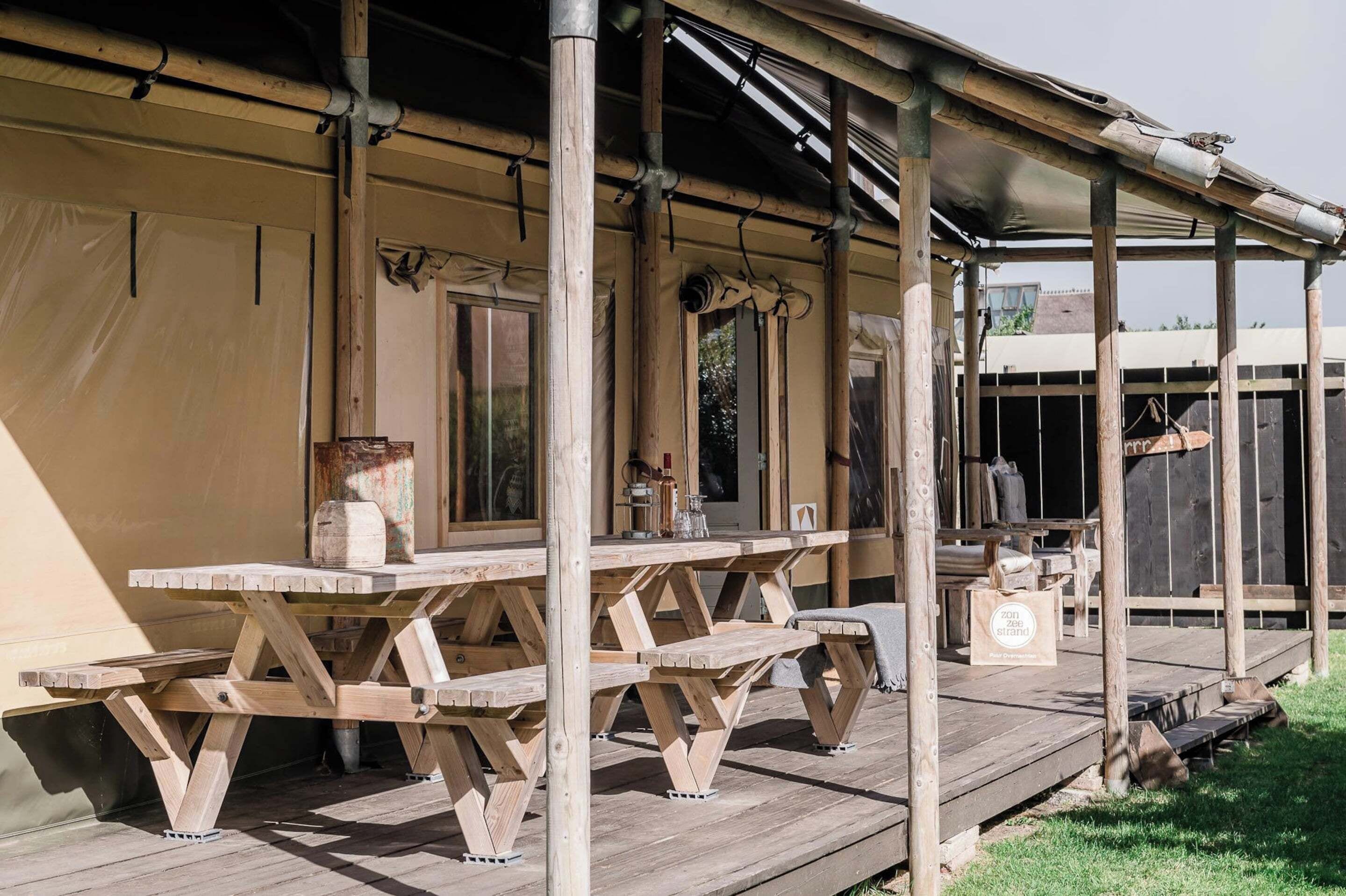 A wooden deck with picnic tables and a covered area with a metal roof.