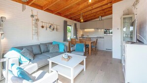 A modern living room with a wooden ceiling, a sofa set, a dining area, and a kitchen. - De Blenck 67 Family-friendly Bungalow (Callantsoog)