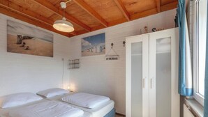 A room with two beds, a white wardrobe, and a painting of a beach scene. - De Blenck 67 Family-friendly Bungalow (Callantsoog)