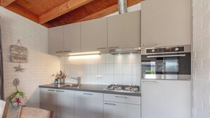 A modern kitchen with white cabinets, stainless steel appliances, and a wooden ceiling. - De Blenck 67 Family-friendly Bungalow (Callantsoog)