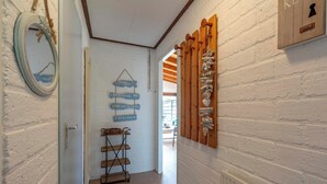 A hallway with a white brick wall, a wooden door frame, and a shelf with decorative items. - De Blenck 67 Family-friendly Bungalow (Callantsoog)