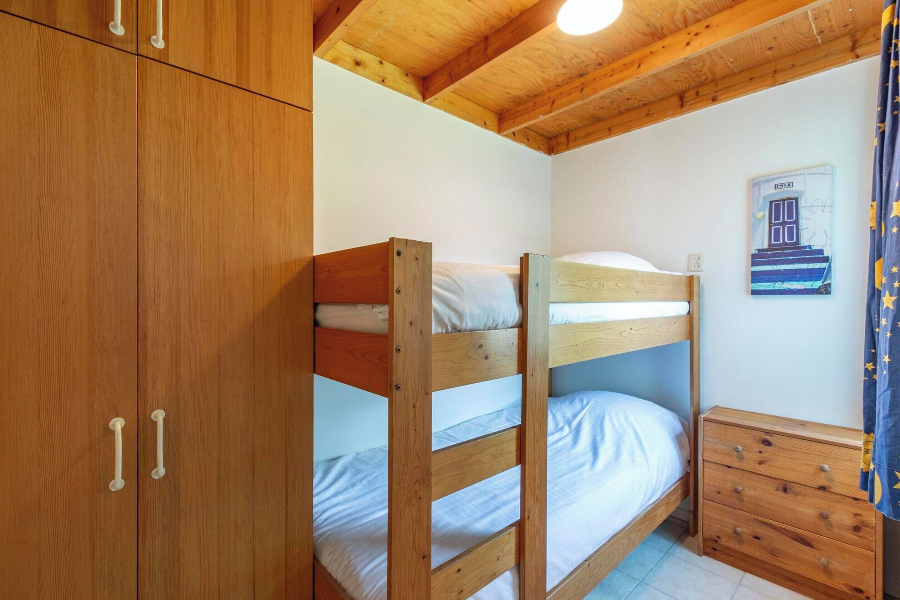 Una cama nido con cabecera de madera, un pequeño aparador de madera y un cuadro colgado en la pared.