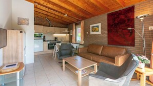 Ein modernes Wohnzimmer mit Holzboden, einer Couch, einem Couchtisch und einer Küche im Hintergrund.