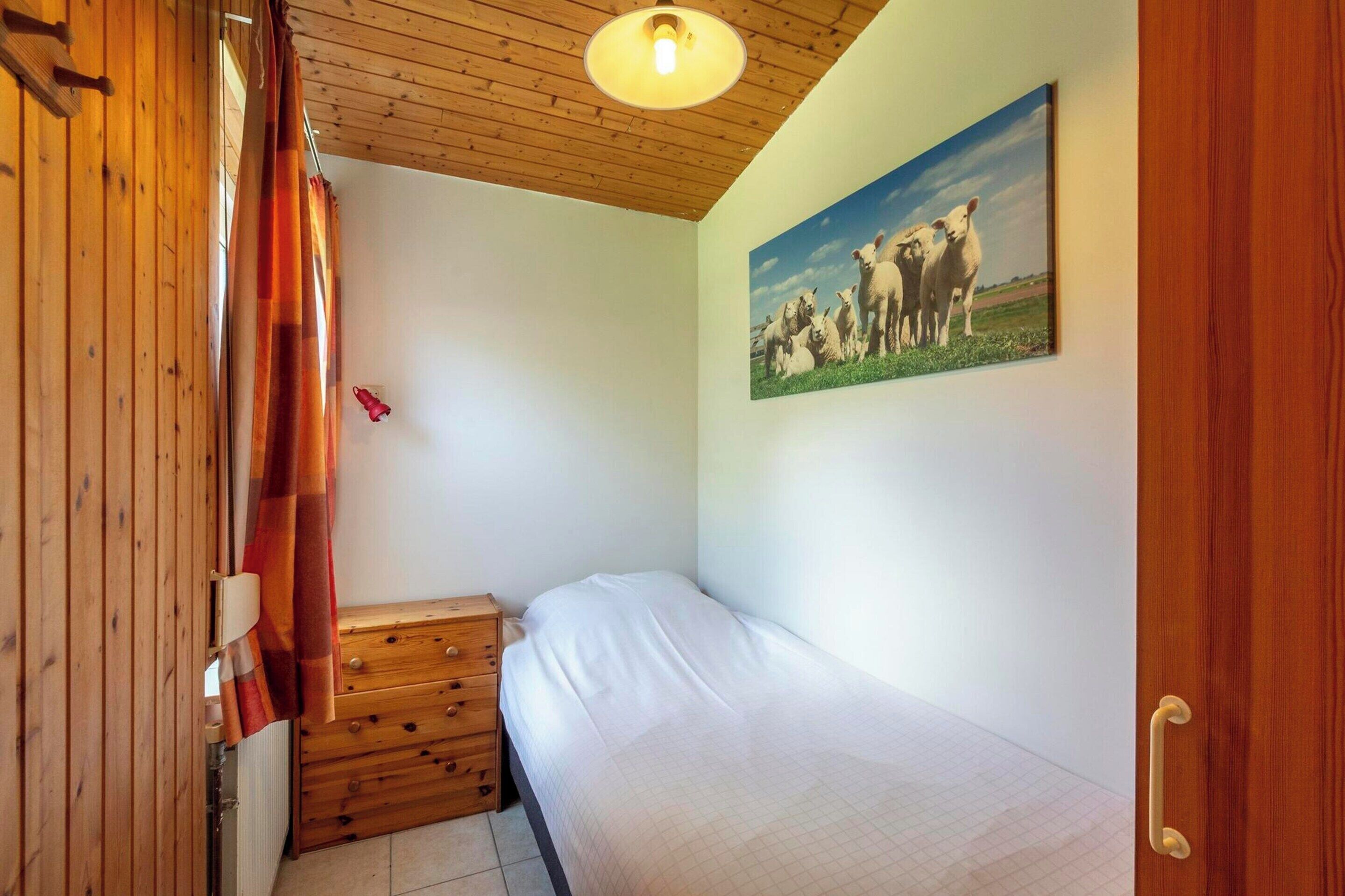 A bedroom with a wooden ceiling, a bed, a dresser, and a painting of cows on the wall.