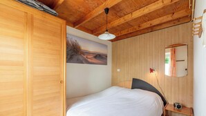 Ein Schlafzimmer mit Holzboden, einem Bett mit weißer Bettwäsche, einem kleinen Nachttischchen mit Radio und einem an der Wand befestigten Spiegel.
