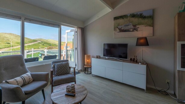 A modern living room with a large window, a flat-screen TV, a lamp, and a painting on the wall. - Beach Apartment 35 for 4 Guests, Callanstoog (Callantsoog)