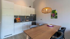 A modern kitchen with white cabinets, a wooden dining table, and a hanging light fixture. - Beach Apartment 35 for 4 Guests, Callanstoog (Callantsoog)