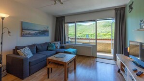 Una sala de estar moderna con sofá, una mesa de centro, un mueble para televisor y un ventanal con vistas a la vegetación.