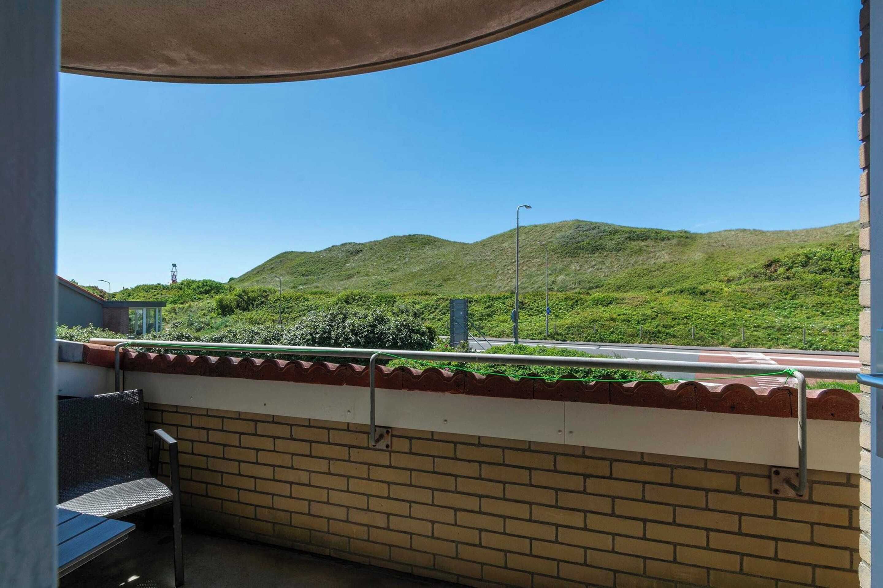 Ein Balkon mit Blick auf grüne Hügel und einen klaren Himmel.