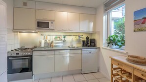 A modern kitchen with white cabinets, a built-in microwave, a gas stove, and a dishwasher. There is a window with a view of greenery outside. - Holiday Home Near Dutch Beach With Pool (Sint Maartensvlotbrug)