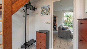 A modern living room with a grey sofa, a wooden staircase, a black coat rack, and a painting on the wall. - Holiday Home Near Dutch Beach With Pool (Sint Maartensvlotbrug)