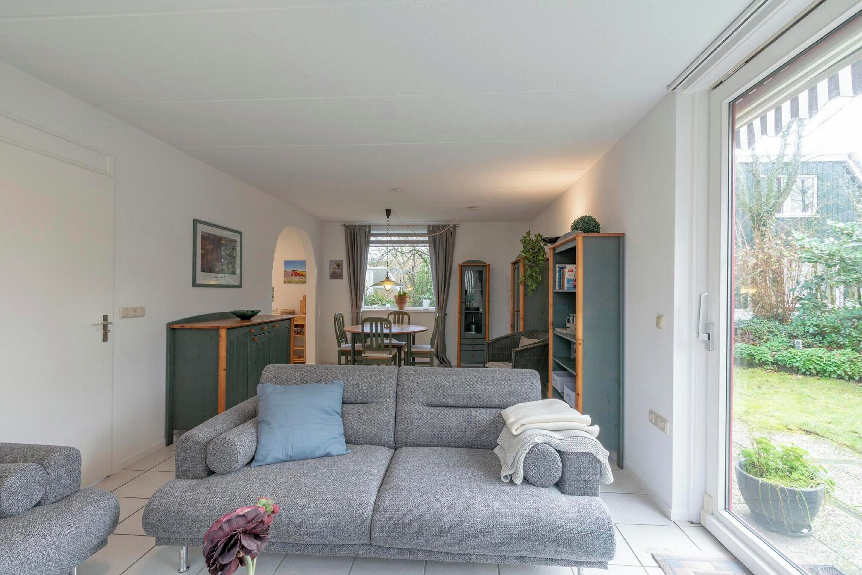 A modern living room with a grey sofa, a small table, and a view of the garden through a large window.