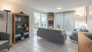 A modern living room with a grey sofa, a wooden coffee table, and a bookshelf. - Holiday Home Near Dutch Beach With Pool (Sint Maartensvlotbrug)