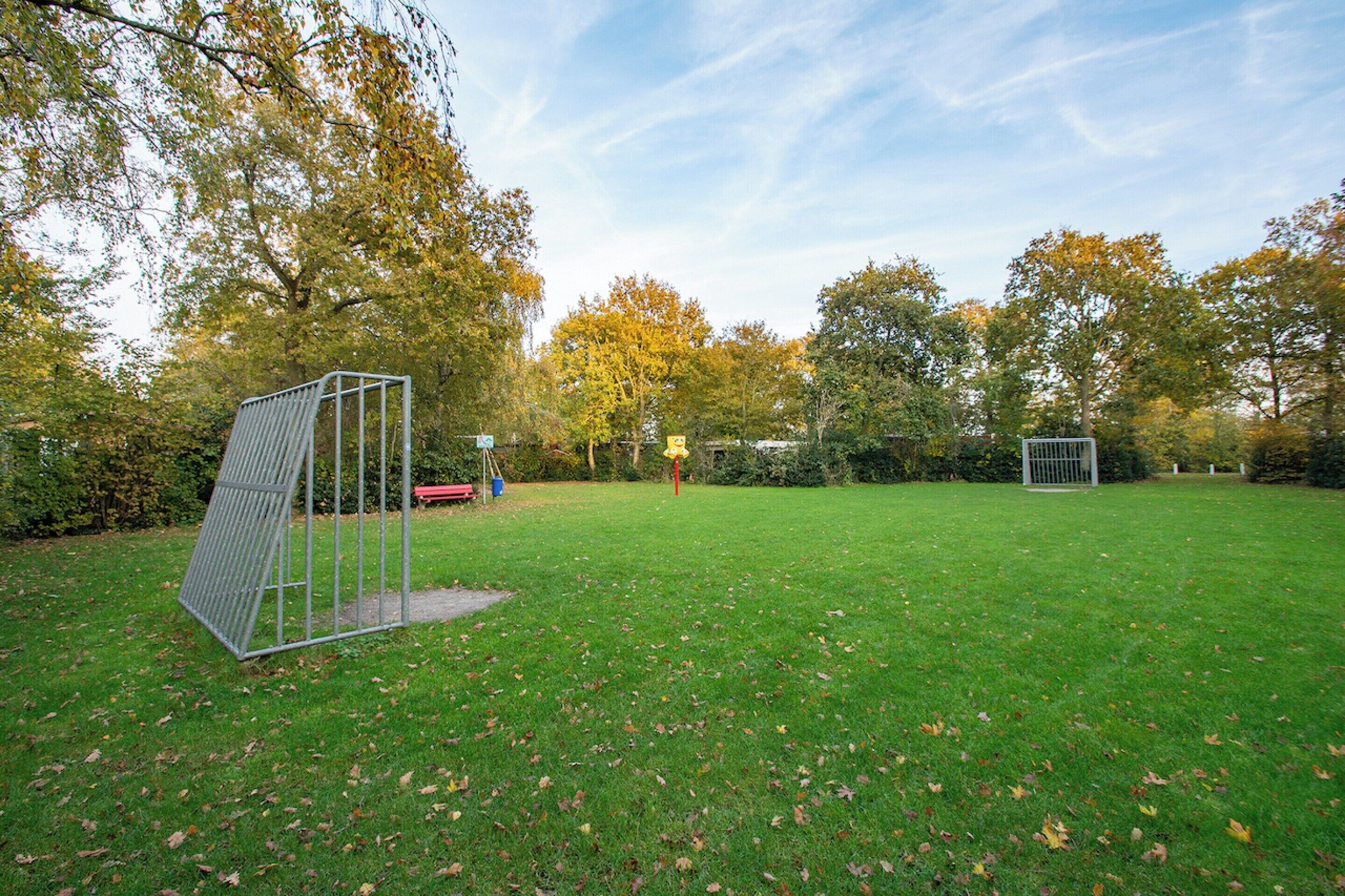 A grassy outdoor area with a metal structure, possibly a play area or garden feature, surrounded by trees with autumn foliage.