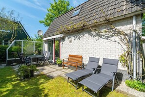 A patio with a table and chairs, a wooden bench, and two lounge chairs. - Holiday Home Near Dutch Beach With Pool (Sint Maartensvlotbrug)