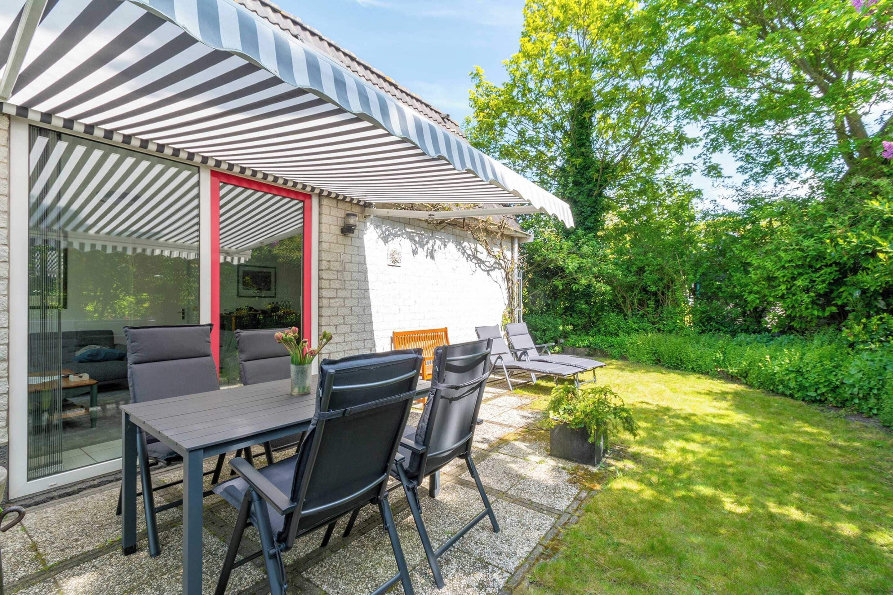 Een terras met tafel en stoelen, een overdekte zithoek en een tuin met gazon en bomen.