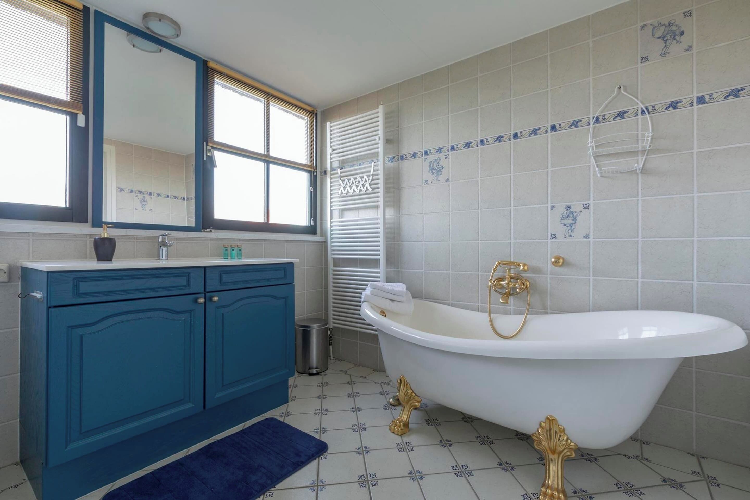 Une salle de bain avec une baignoire blanche, des meubles bleus, un miroir et des carreaux à motifs.