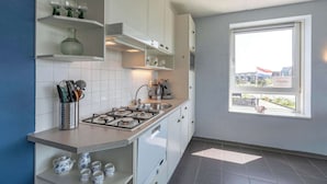 A modern kitchen with white cabinets, a gas stove, and a window with a view of buildings. - Callantsduyne 21 With Groote Keeten Dune View (Callantsoog)