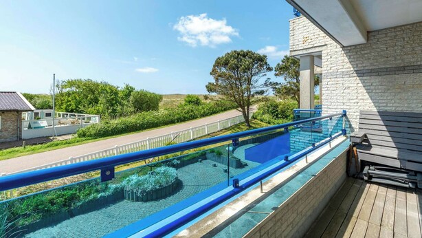 A pool area with a blue railing, a stone wall, and a view of the surrounding landscape. - Callantsduyne 21 With Groote Keeten Dune View (Callantsoog)
