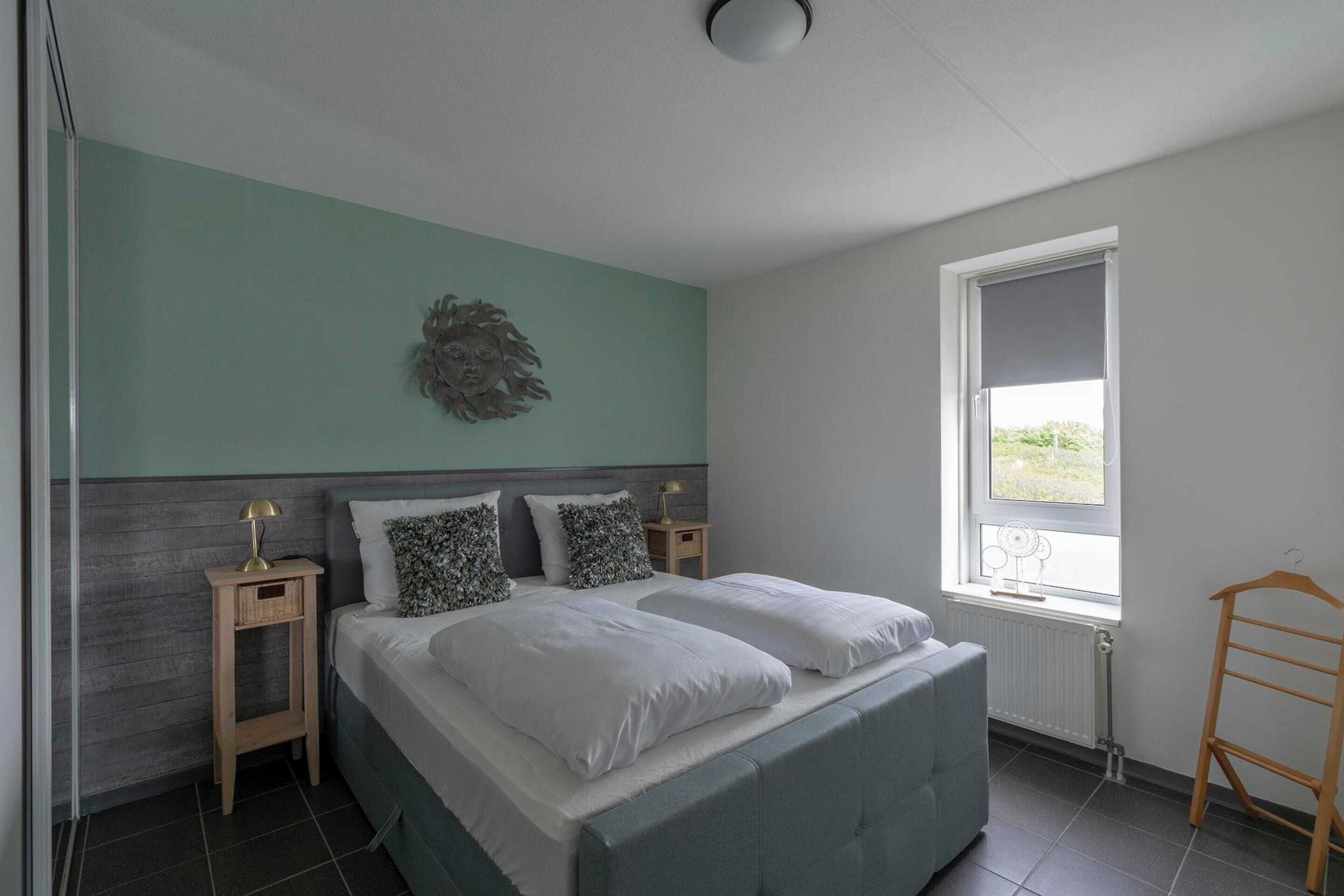 A bedroom with a bed, two bedside tables, a window, and a radiator.