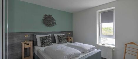 A bedroom with a bed, two bedside tables, a window, and a radiator.