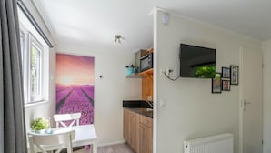 A compact living space with a dining area, kitchenette, and a large window with curtains. - Chalet in Texel Near Beach and Forest (Sint Maartensvlotbrug)