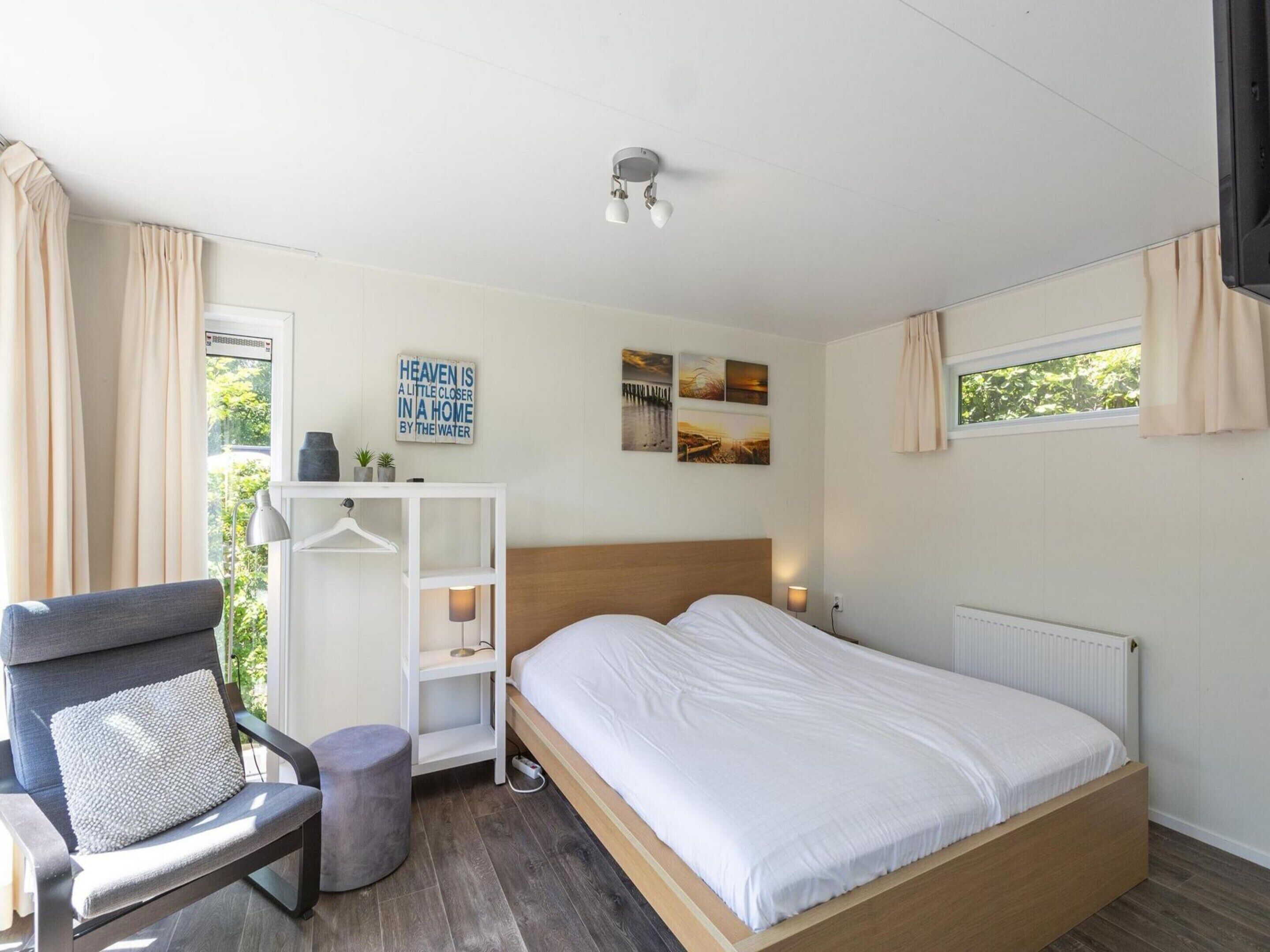 Ein Schlafzimmer mit einem Bett, einem Sessel, einem kleinen Tisch, einem Regal, einem Fenster und einer Wand mit einem Schild.