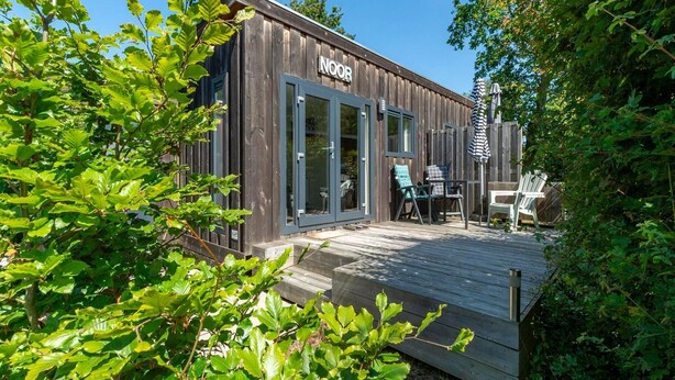 A wooden building with a sign reading 'NOR' and a deck with chairs. - Chalet in Texel Near Beach and Forest (Sint Maartensvlotbrug)