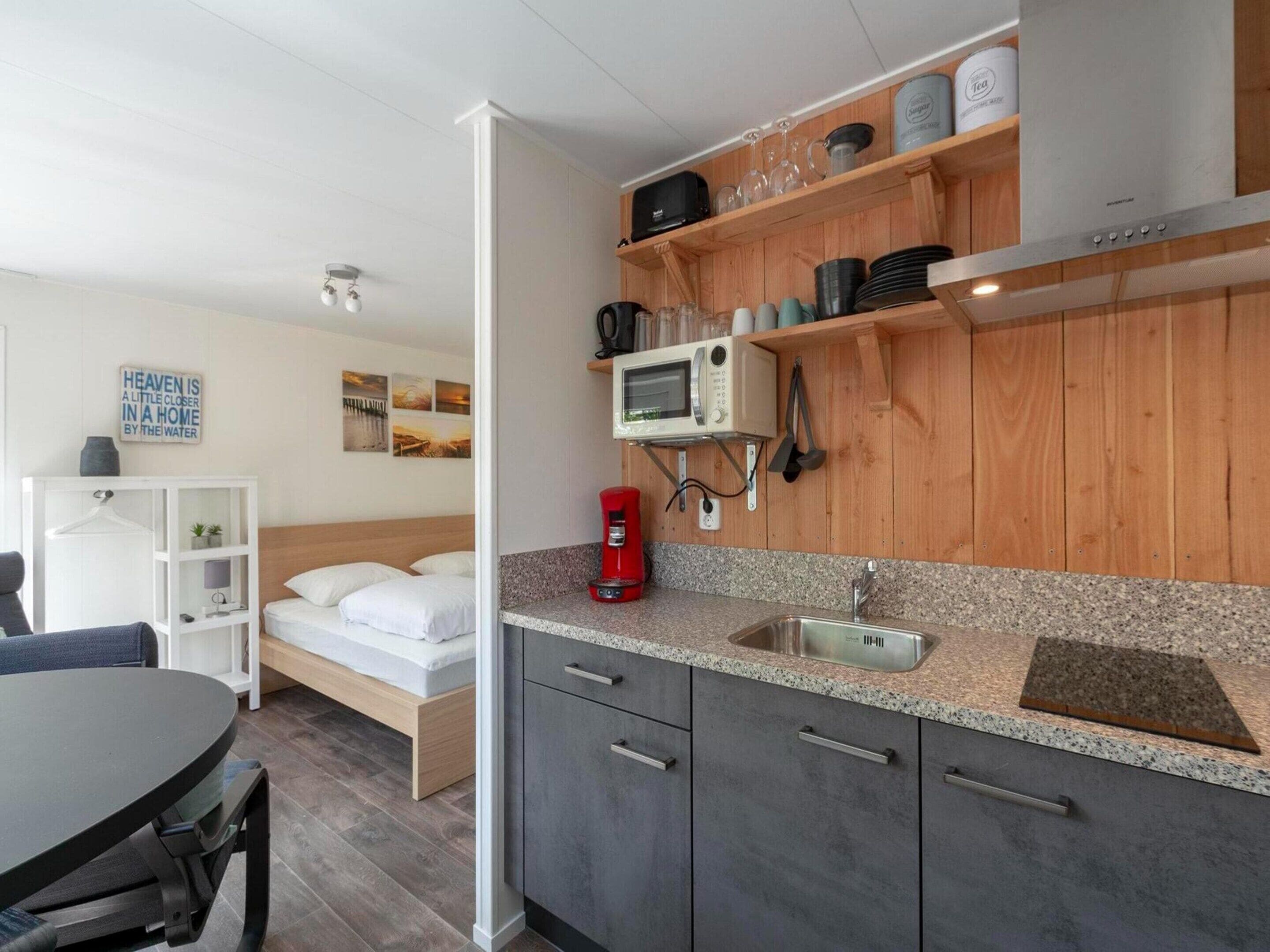 A compact kitchen with a microwave, coffee maker, and wooden shelves.