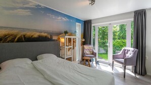 A bedroom with a large bed, a desk with a chair, and a view of the outdoors through a sliding glass door. - Chalet in Texel Near Beach and Forest (Sint Maartensvlotbrug)