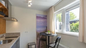 A compact kitchen with granite countertops, a stainless steel sink, a small trash bin, and a dining area with a table and chairs. - Chalet in Texel Near Beach and Forest (Sint Maartensvlotbrug)