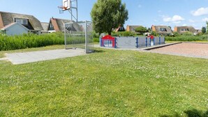 A residential area with a basketball hoop, a gated playground, and houses with sloped roofs. - Villa With View Over the Park De Buitenplaats (Callantsoog)