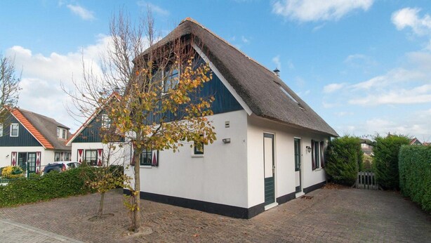 A single-story house with a steeply pitched roof, a small front porch, and a brick driveway. - Villa With View Over the Park De Buitenplaats (Callantsoog)