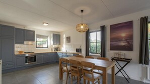 A modern kitchen with grey cabinets, a dining table with chairs, and a pendant light. - Villa With View Over the Park De Buitenplaats (Callantsoog)