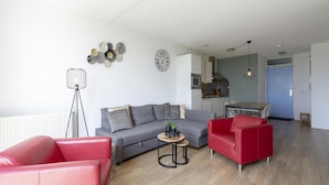 A modern living room with a grey sofa, red armchairs, a small coffee table, and a kitchen in the background. - Apartment Near Groote Keeten Beach (Callantsoog)
